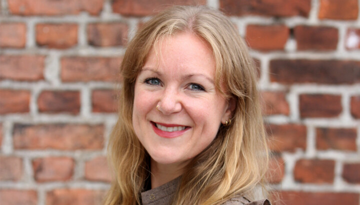 Sofie Dege Dimmen, seniorrådgiver kommunikasjon i Nærings- og fiskeridepartementet. Foran en murvegg, smilende.