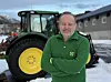 Mann i grønn John Deere-genser foran grønn og gul traktor på snødekt gårdsplass