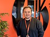 En mann med nøkkelbånd står foran en oransje vegg og svarte former i et moderne rom.