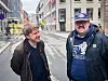 Anders Muurman Holm og Svein Werner Lyngmyr står i en regnvåt bygate med bygninger og trafikkilt i bakgrunnen.
