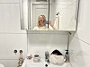 Person tar selfie foran speilet på et hvitt bad med servant og toalettartikler.