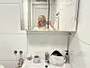 Person tar selfie foran speilet på et hvitt bad med servant og toalettartikler.