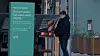 Person ved en ladestasjon for elbil ved siden av en grønn infosøyle.