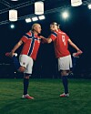 To fotballspillere i røde drakter feirer på gressbanen under sterke stadionlys.