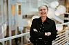 Smilende kvinne i svart blazer står med armene i kors i et lyst, moderne lokale.