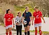 Fire fotballspillere går langs en sti og holder fotballer.