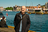 En mann står på en brygge foran en havn med båter og bygninger.