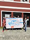 To personer holder et stort kart foran en rød bygning med butikkvindu.