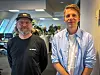 To menn står i et moderne kontor med åpne arbeidsplasser og planter i bakgrunnen.