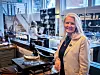 Lise-Karin Redfern står ved en Arven 1868-utstilling med historiske kjøkkenredskaper i et lyst lokale.