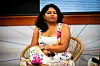 Aarti Bhaskaran sitter i en flettet stol på en scene med mikrofon i fanget.