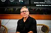 Les Binet sitter i et studio med mørk skjorte, stolene og en skjerm synlige i bakgrunnen.