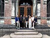 Seks personer står foran en historisk bygning med stor tredør og trapp.