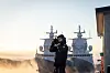 En soldat står foran to krigsskip i havn i morgensol med tåke over vannet.