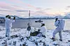 Tre personer i hvite vinterdrakter ved en korvett under skyteøvelse ved sjøen.