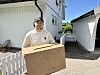 Person står i sollys og holder et pappskilt foran hvite bygninger i en trang gårdsplass.