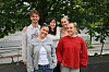 Fem unge voksne står samlet foran en bygning med trær og busker i forgrunnen.