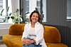 Kvinne sitter på en gul sofa i et lyst kontor med planter og glassvegger.