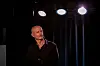 Harald Eia står på en opplyst scene foran svarte gardiner og sterke scenelys.