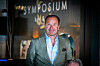 Lars Erik Grønntun foran en symposiumbakgrunn, iført grågrønn dressjakke og lyseblå skjorte.