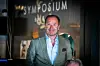 Lars Erik Grønntun foran en symposiumbakgrunn, iført grågrønn dressjakke og lyseblå skjorte.