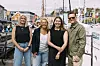 Fire personer står sammen på en marina med båter og brygger i bakgrunnen.