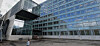 Moderne bygning med blå glassfasade og fotgjengere på en åpen plass.
