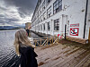 Person på bryggepromenade ved en hvit bygning, vann og fjell i bakgrunnen.