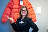 Kristina Skogen i svart blazer foran en rød dunjakke på veggen.