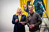 To menn står foran et fargerikt kunstverk, med en stige og en annen person synlig i bakgrunnen.