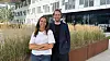 To personer står foran et moderne kontorbygg med høyt gress i plantekasser.