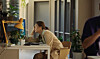 Person ved arbeidsbord i lyst kontor med planter og gul lampe