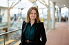 Trude Luise Nedregård Isaksen står i en moderne, lys gang med glassvegger.
