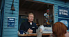 Ansatt betjener en kunde gjennom luka i en blå kiosk.